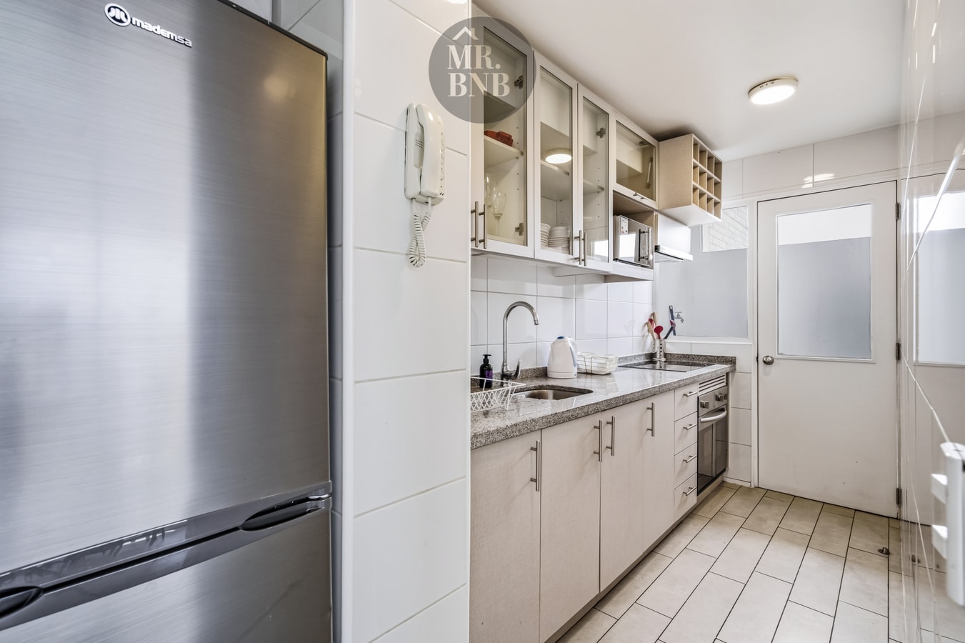 Cocina con refrigerador de acero, muebles altos vidriados y mesón con lavaplatos