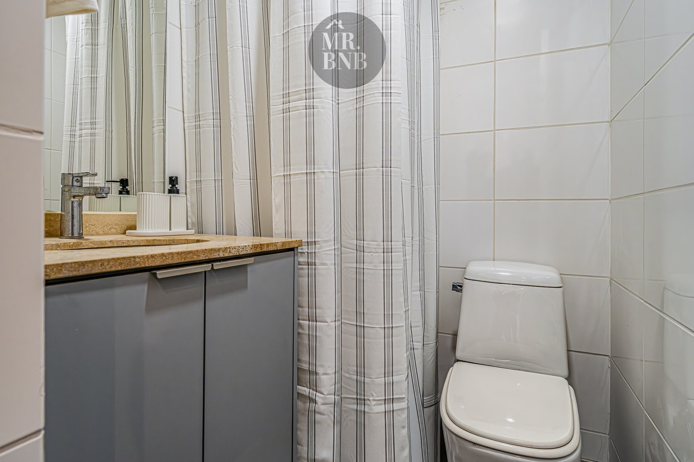 Baño con lavamanos sobre mueble, cortina de baño a rayas e inodoro