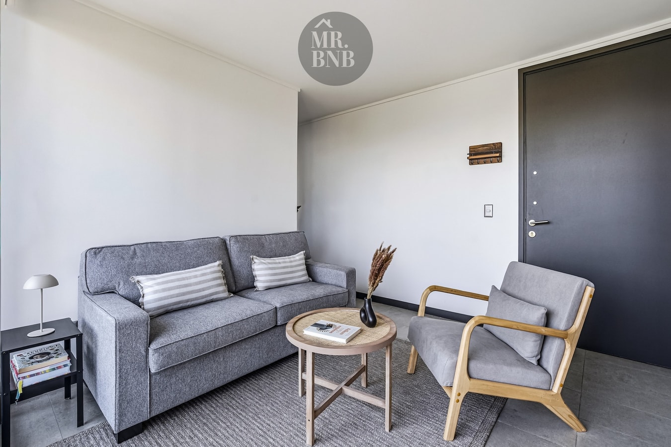 Living con sofá gris, sillón y mesa de centro, junto a la puerta de acceso