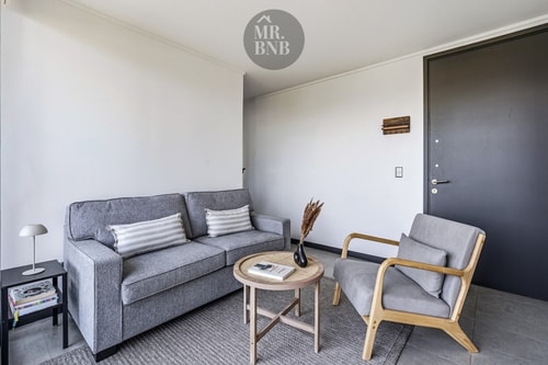 Living con sofá gris, sillón y mesa de centro, junto a la puerta de acceso