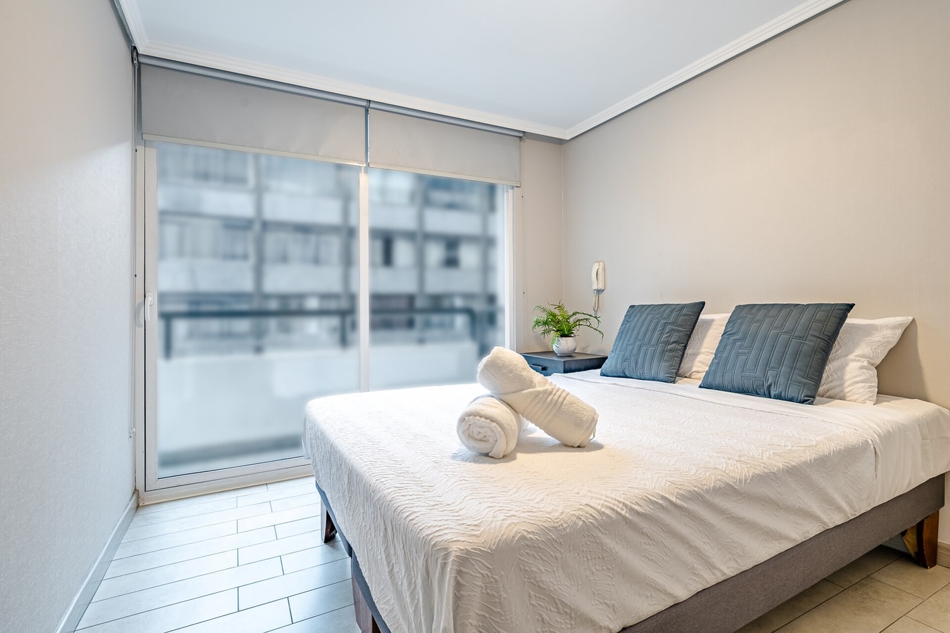 Dormitorio con cama doble, cojines azules y ventana con persiana.