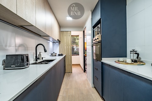 Cocina en galería angosta, muebles azul oscuro y blanco, piso flotante
