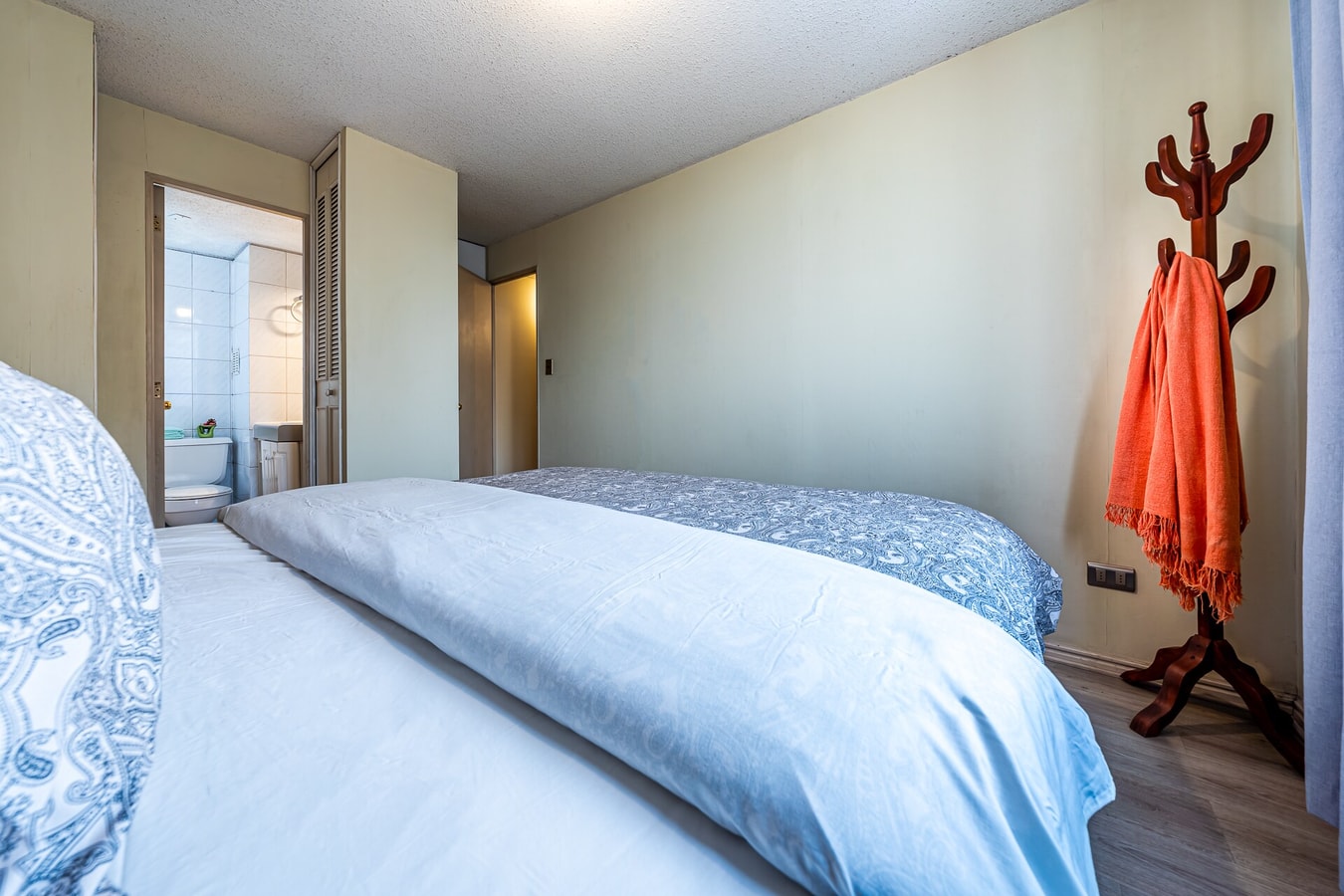 Dormitorio con cama y perchero de pie junto a la puerta de entrada a la pieza.