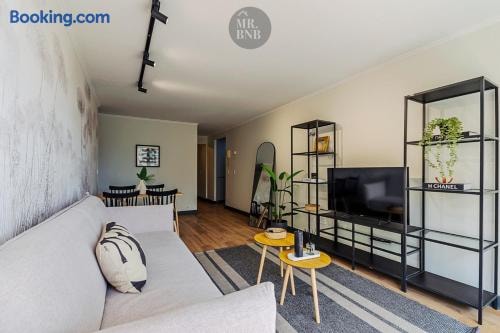 Living con sofá, mueble bajo con televisor y repisa metálica con plantas.