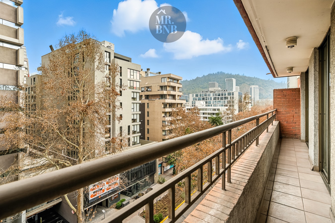 Vista desde el balcón hacia edificios del barrio y cerros al fondo, con día despejado