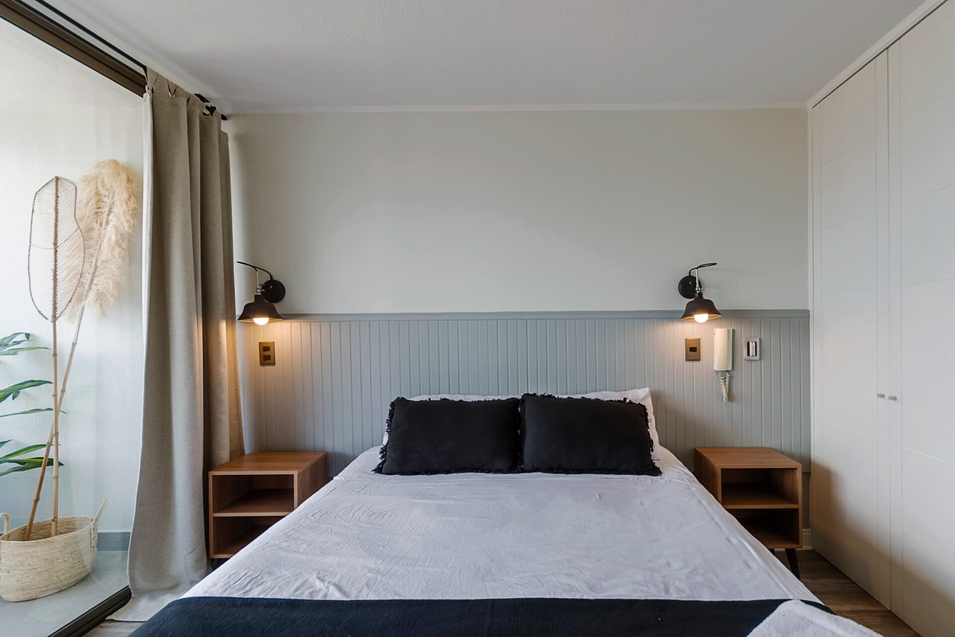 Dormitorio con cama, veladores, cortina, planta seca y closet