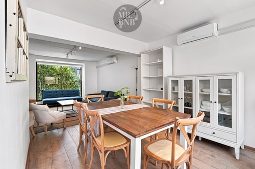 Mesa de madera para 8 con vitrina de loza, aire acondicionado y ventanal al patio con árboles.