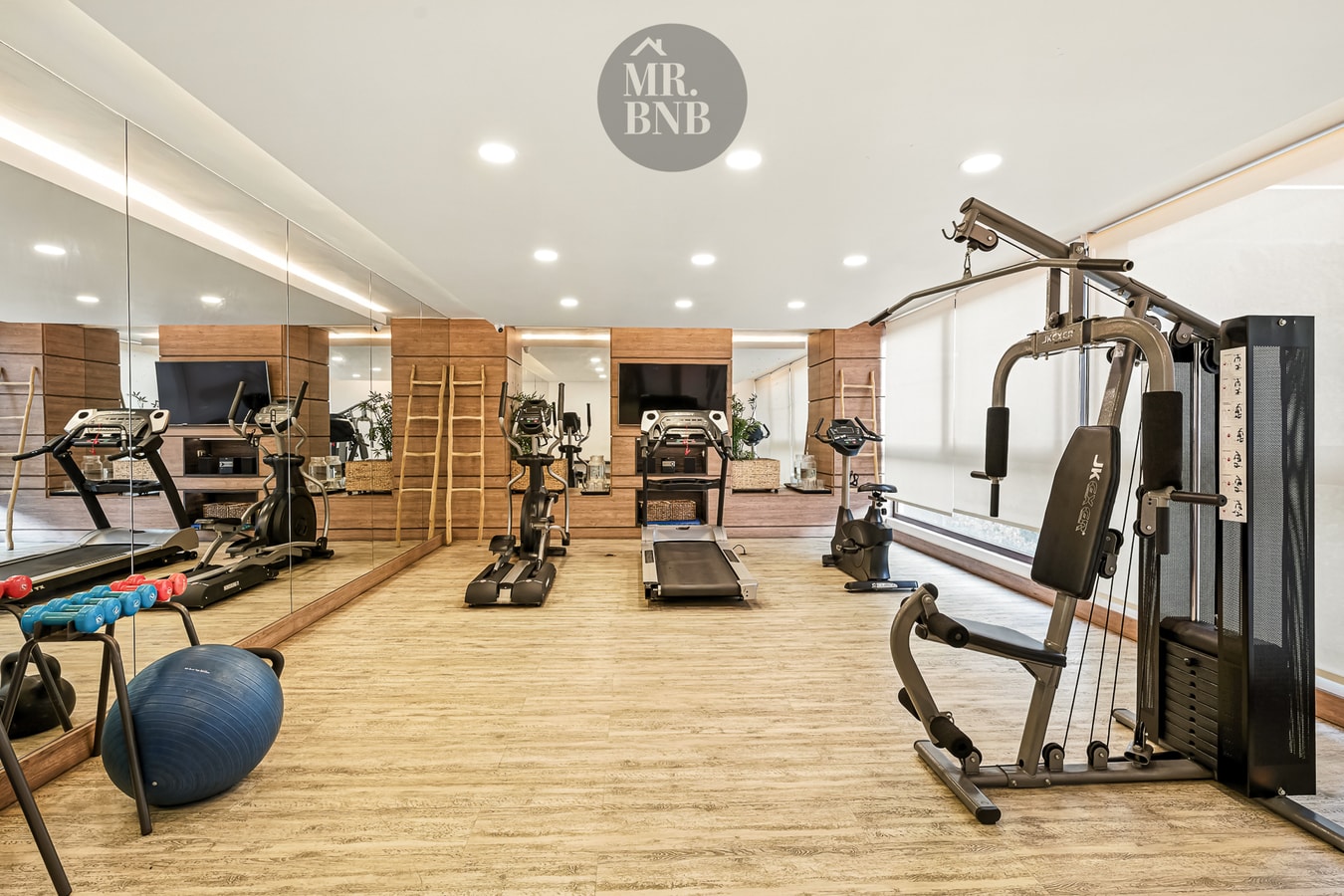 Gimnasio del edificio con máquinas de musculación, trotadora y espejos.