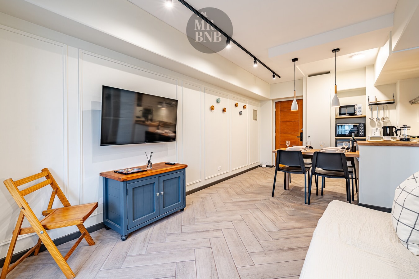 Living con sofá blanco, TV, mueble bajo azul y comedor al fondo con mesa y sillas