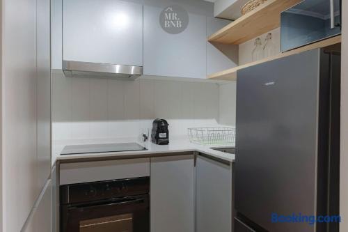 Cocina en L con encimera eléctrica, horno, cafetera y refrigerador.