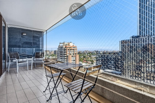 Terraza con mesa y dos sillas, malla de seguridad y vista panorámica de la ciudad.