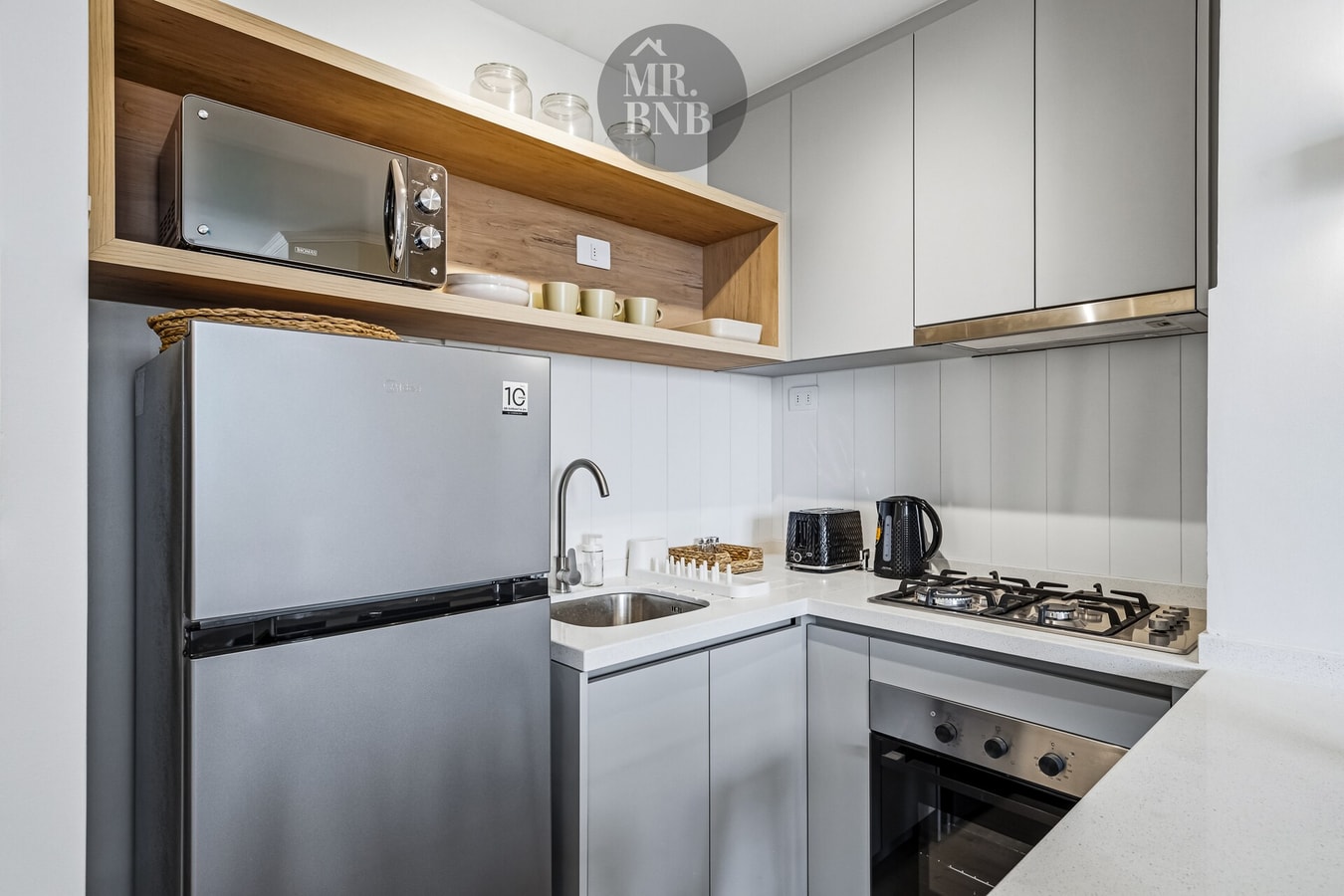 Cocina equipada con refrigerador, cocina a gas, campana y microondas sobre repisa