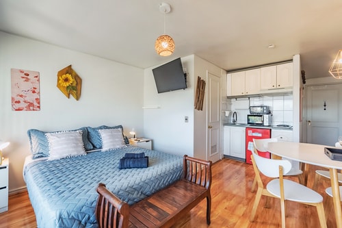 Estudio con cama, mesa de comedor, sillas y kitchenette al fondo