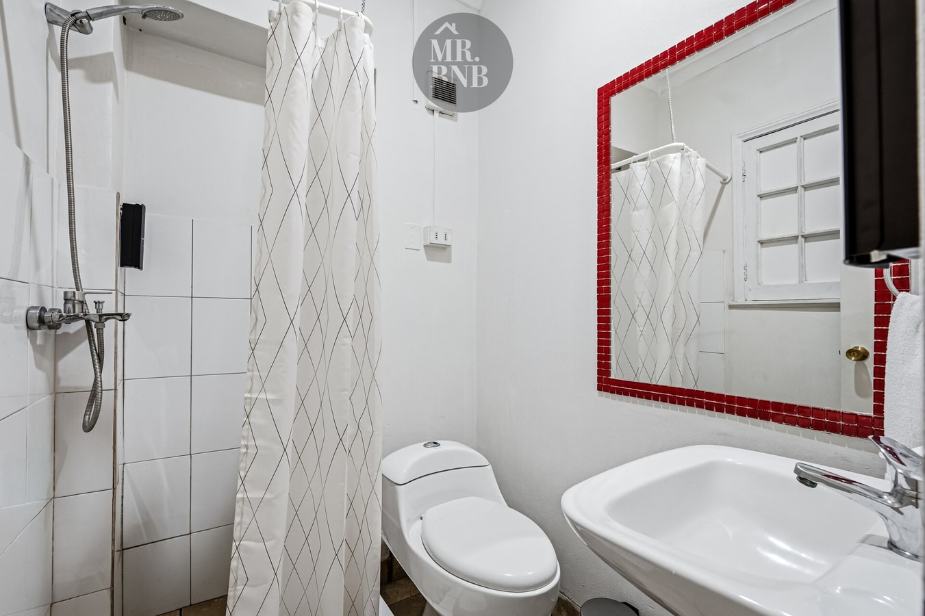 Baño con ducha con cortina, marco de espejo rojo y azulejos blancos.