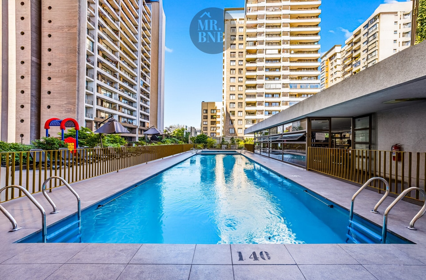 Piscina exterior del edificio con juegos infantiles al fondo y torres circundantes