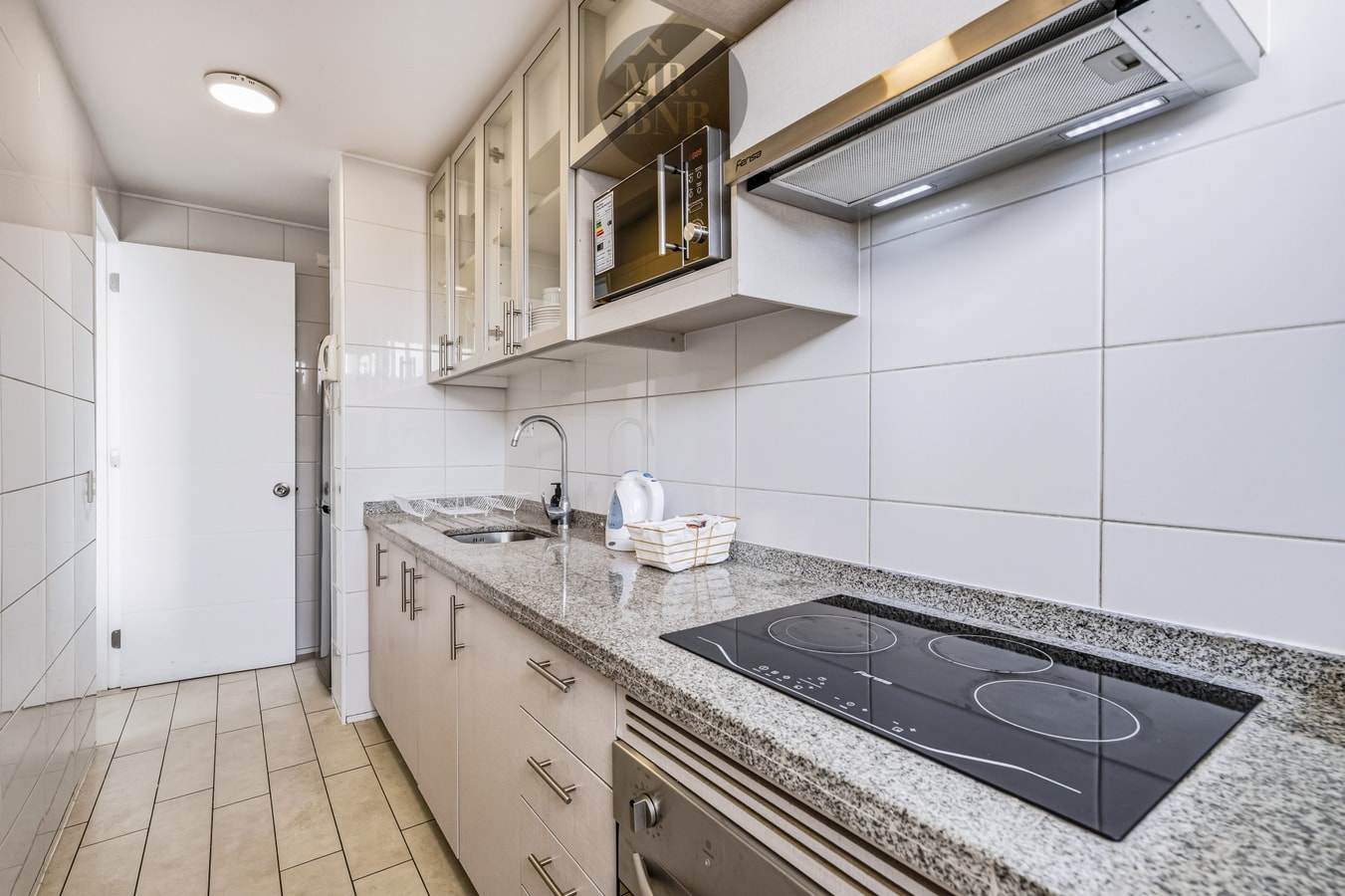 Cocina con encimera eléctrica, horno, campana extractora y muebles altos