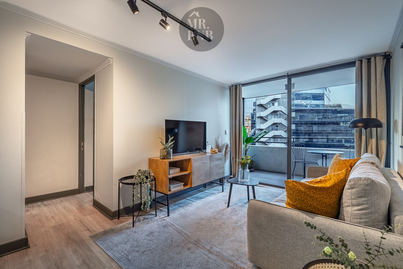 Living con sofá gris, mesa de centro, TV y puerta corredera de vidrio hacia la terraza