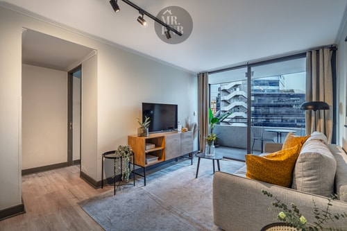 Living con sofá gris, mesa de centro, TV y puerta corredera de vidrio hacia la terraza