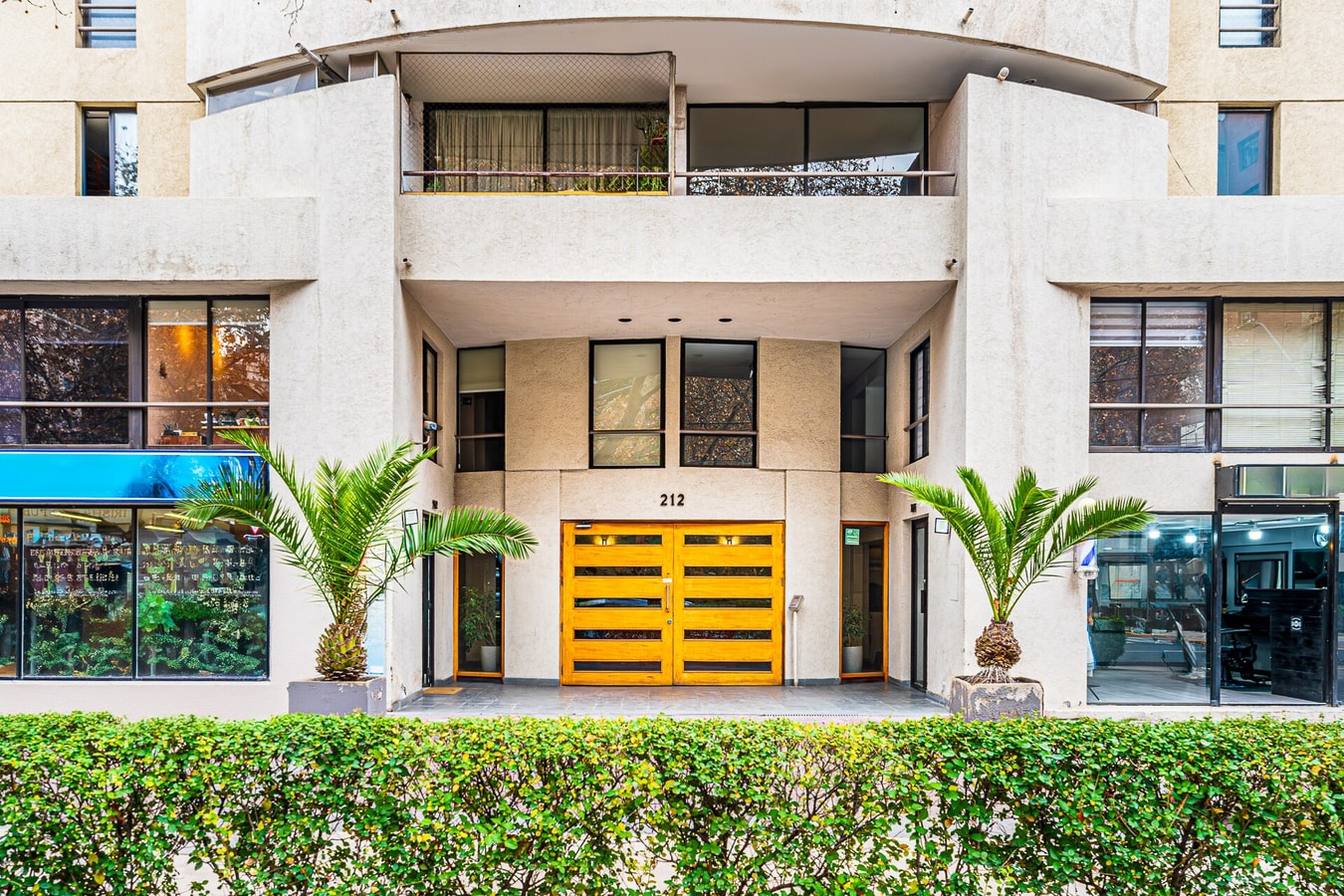 Fachada de acceso del edificio con palmeras y puerta corredera amarilla, vista más amplia
