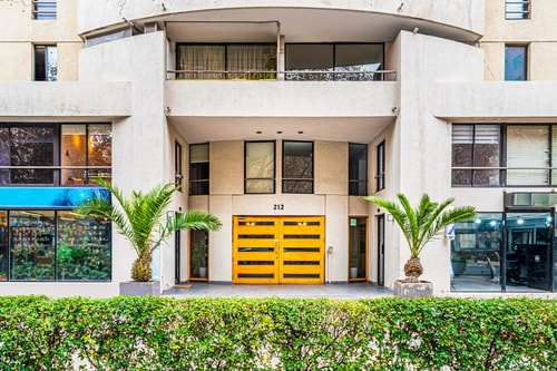 Fachada de acceso del edificio con palmeras y puerta corredera amarilla, vista más amplia