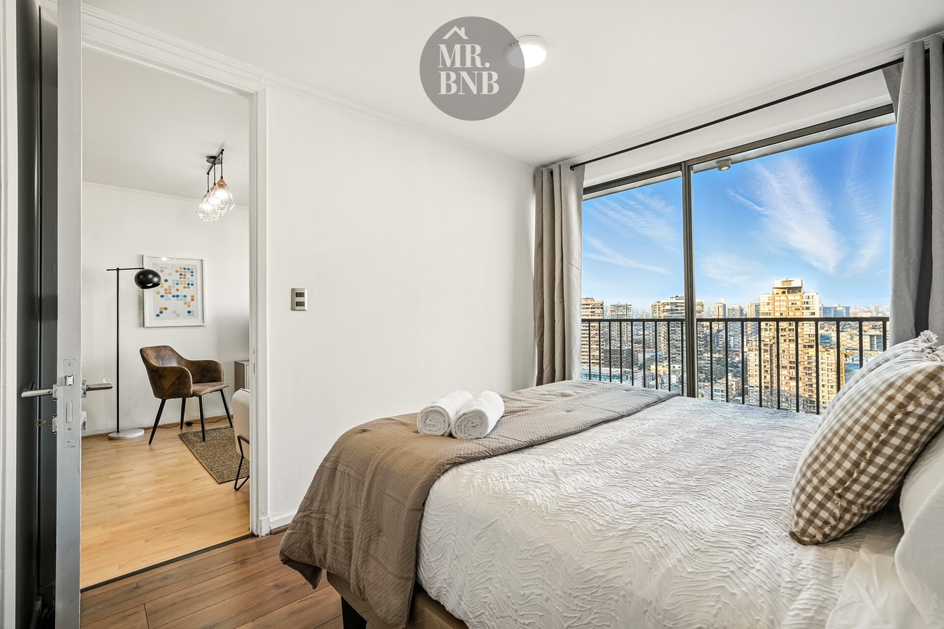 Dormitorio con cama doble, ventanal con vista a la ciudad y acceso a zona de escritorio