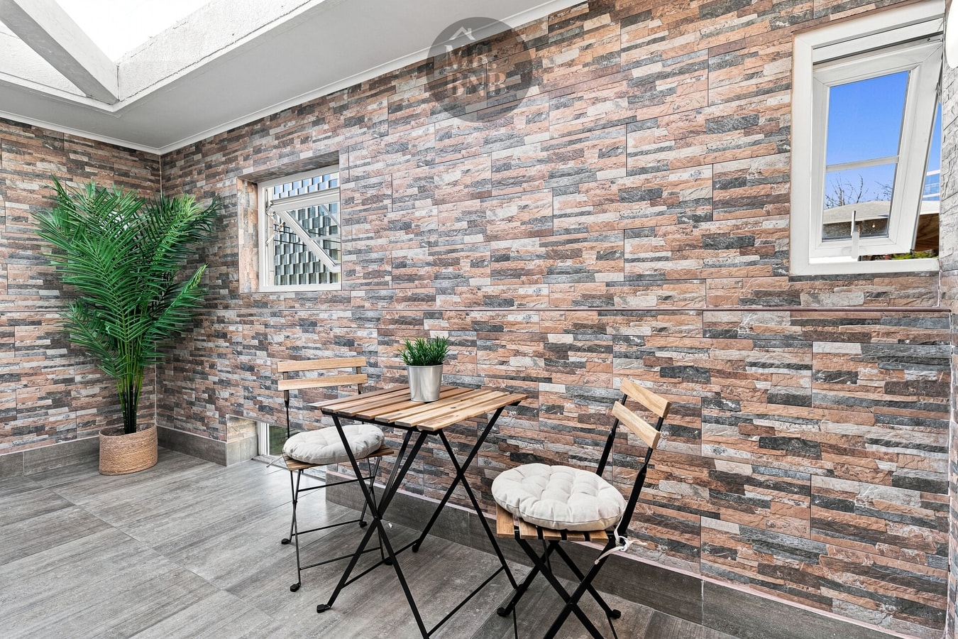 Terraza techada con mesa pequeña, dos sillas, plantas y lucarnas