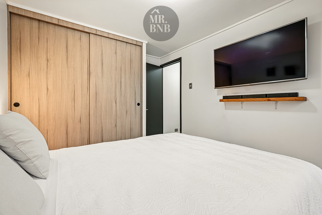 Dormitorio con cama, closet de madera corredizo y televisor en la pared.