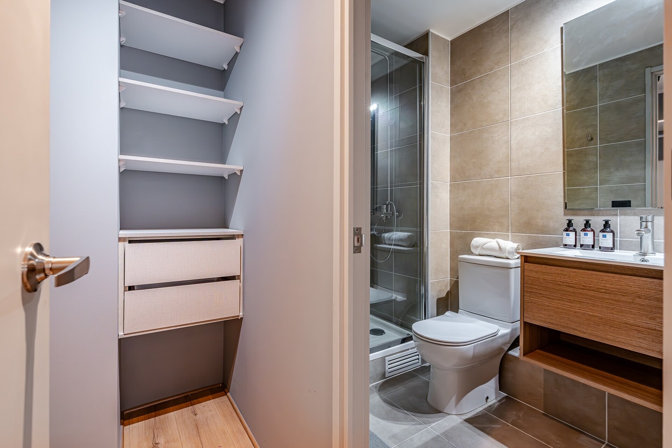 Closet con repisas junto a la puerta de un baño con ducha e inodoro.