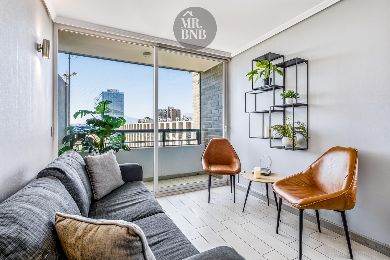 Living con sofá, sillones de cuero, mesa auxiliar y ventanal hacia balcón con plantas