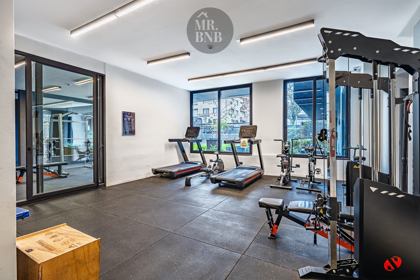 Gimnasio del edificio con máquinas de musculación, cinta de correr y ventanales con luz natural