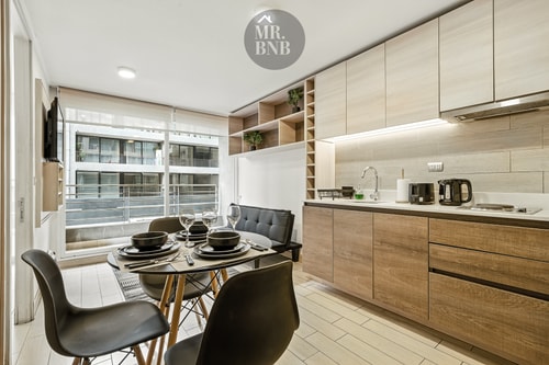 Cocina de madera con mesa de comedor y sillas negras junto a la ventana.