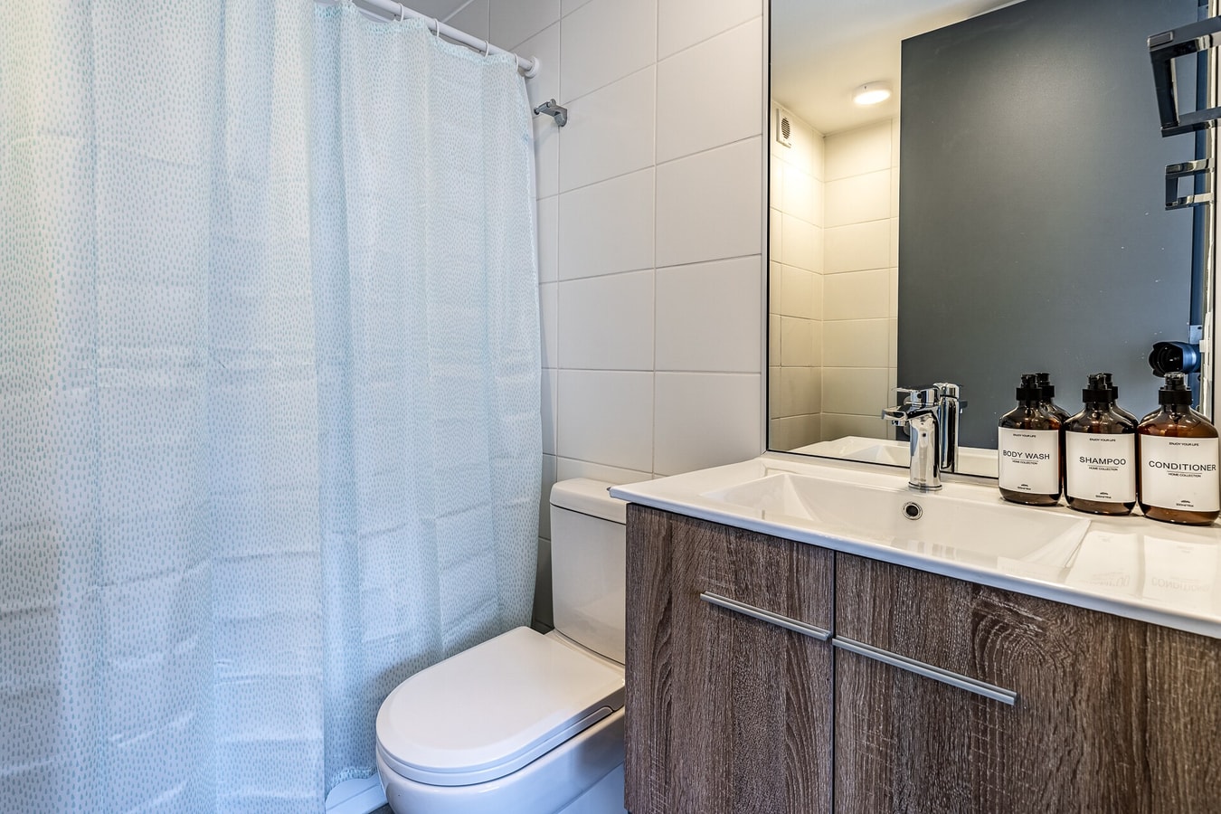 Baño con cortina de ducha, inodoro y lavamanos con espejo de pared.