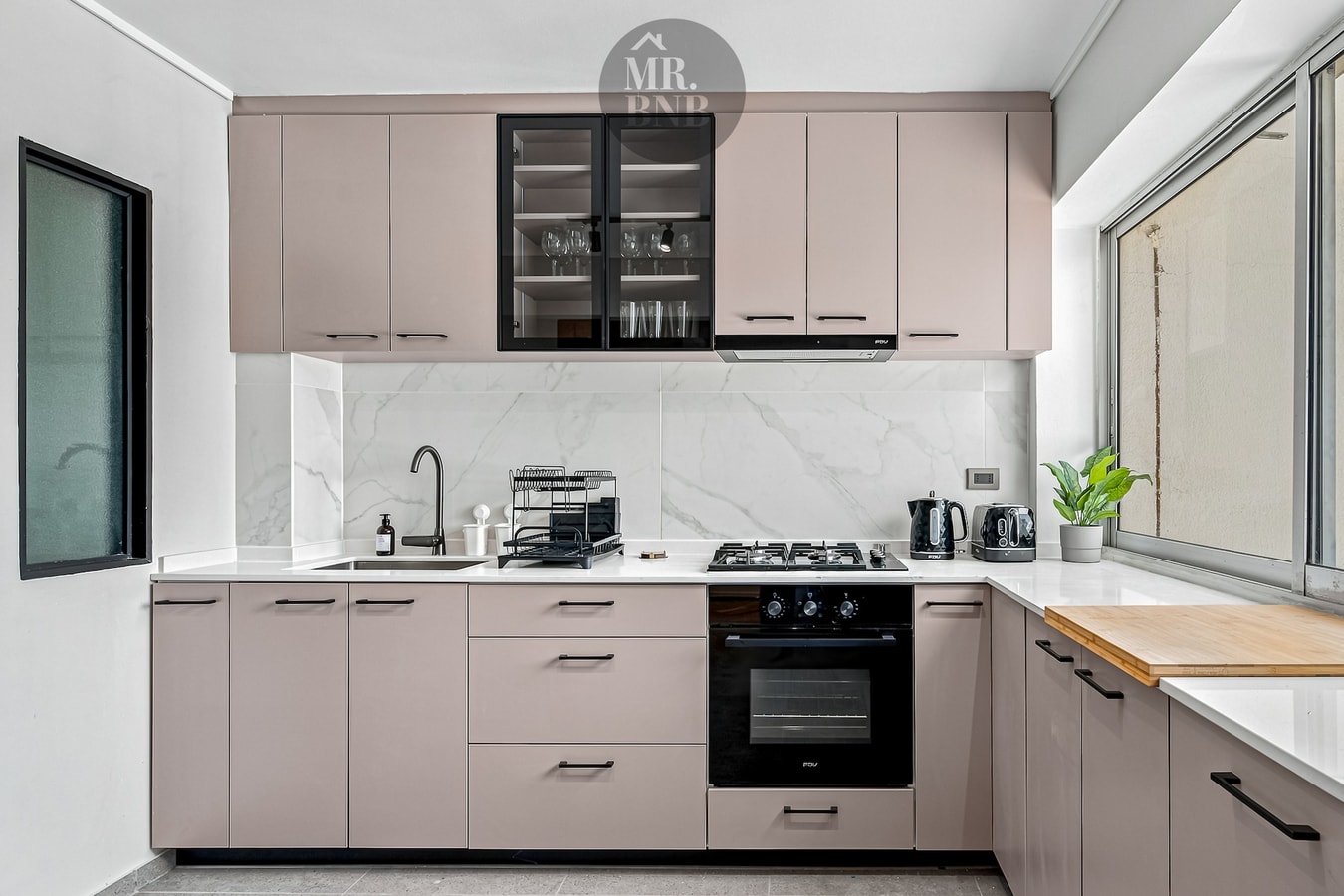 Cocina con muebles rosados, encimera a gas, horno, campana y ventanal