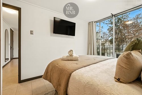 Dormitorio con cama de dos plazas y toallas dispuestas sobre ella, ventanal amplio con cortina
