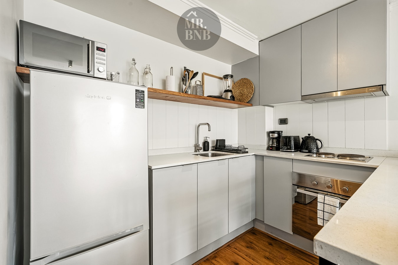 Cocina en detalle con microondas, refrigerador, repisa y muebles blancos