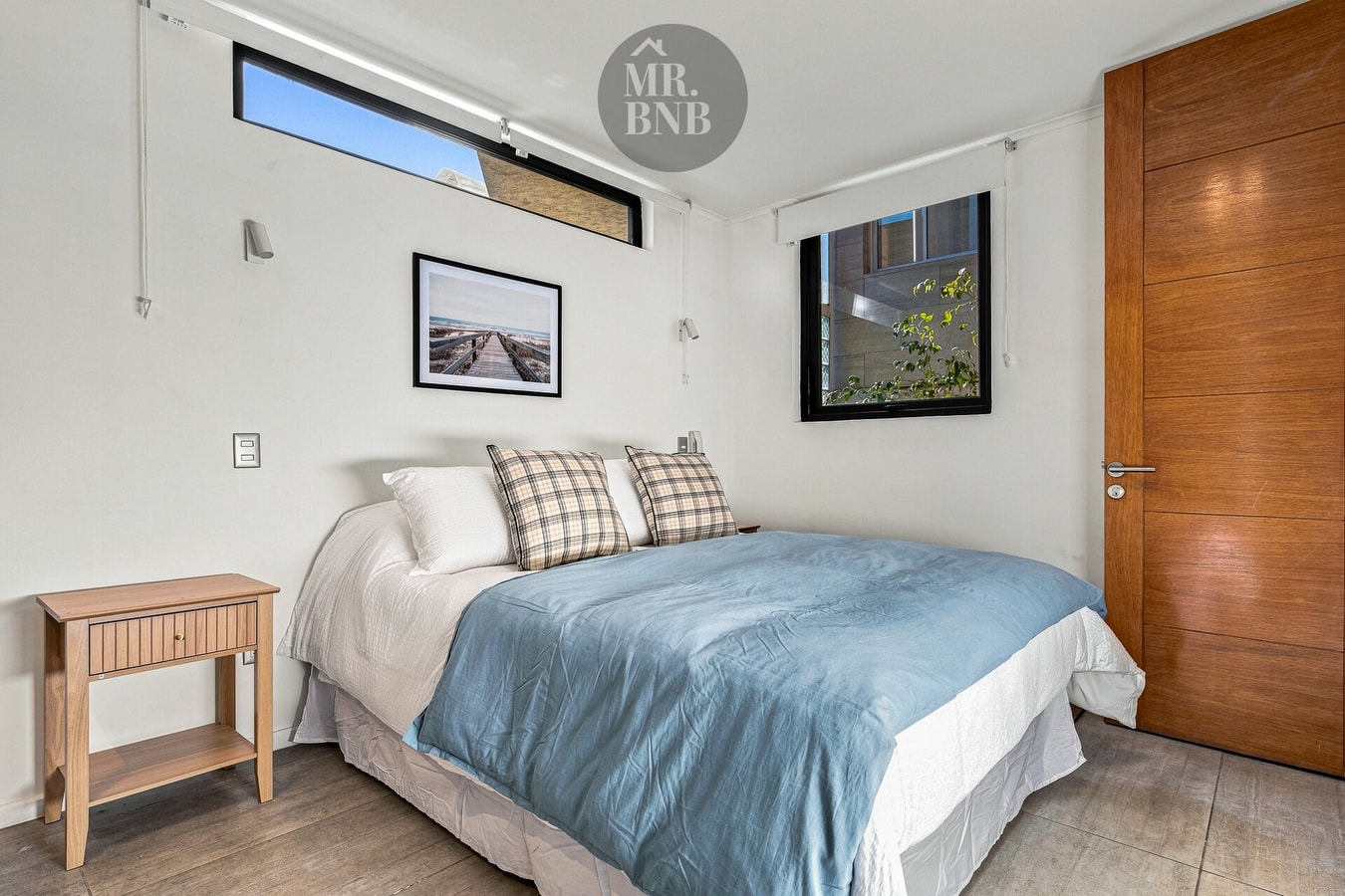 Dormitorio con cama, cubrecama celeste, veladores, puerta de madera y cuadros
