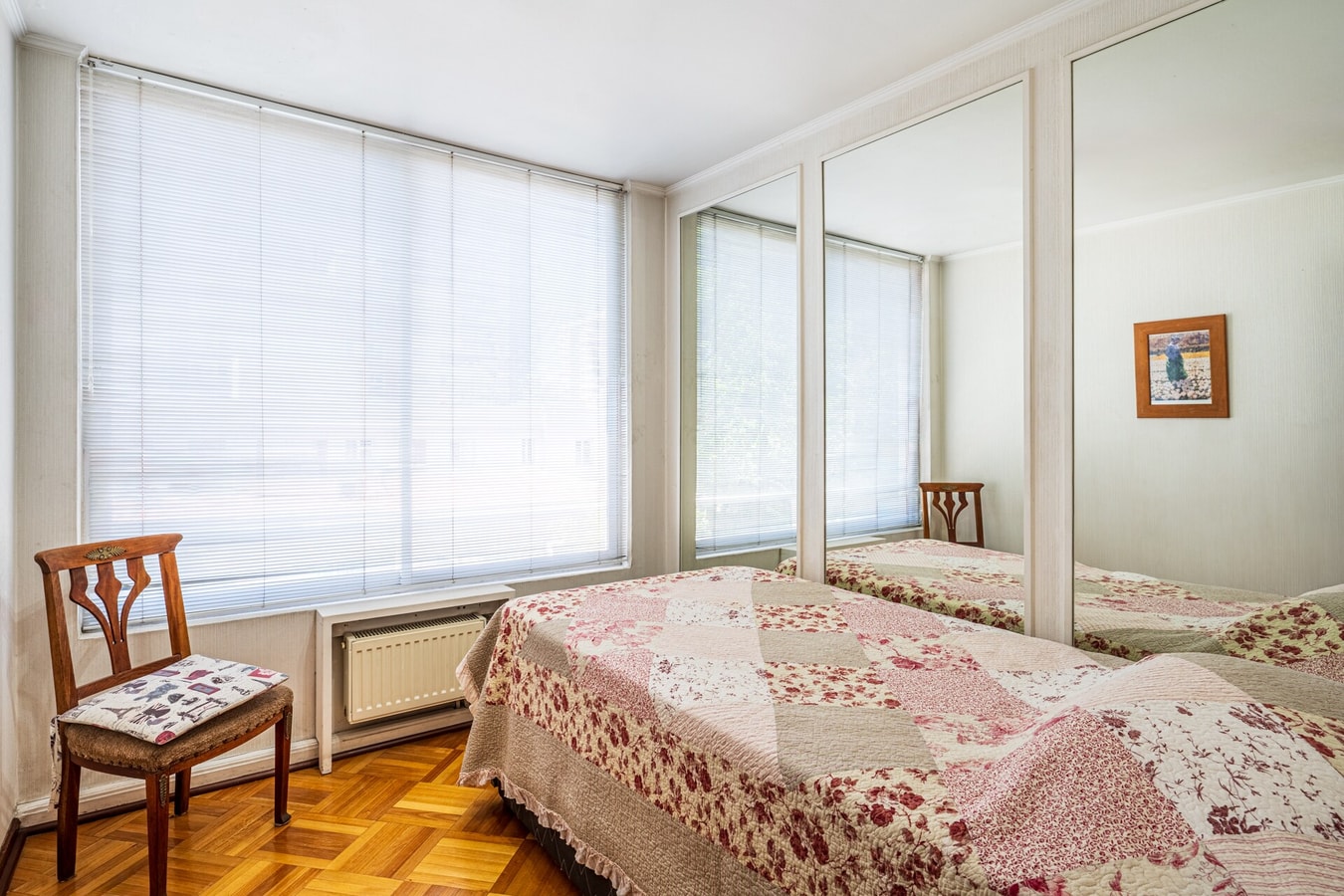 Dormitorio con cama individual, ventana con persianas, clóset con espejo y silla de madera.