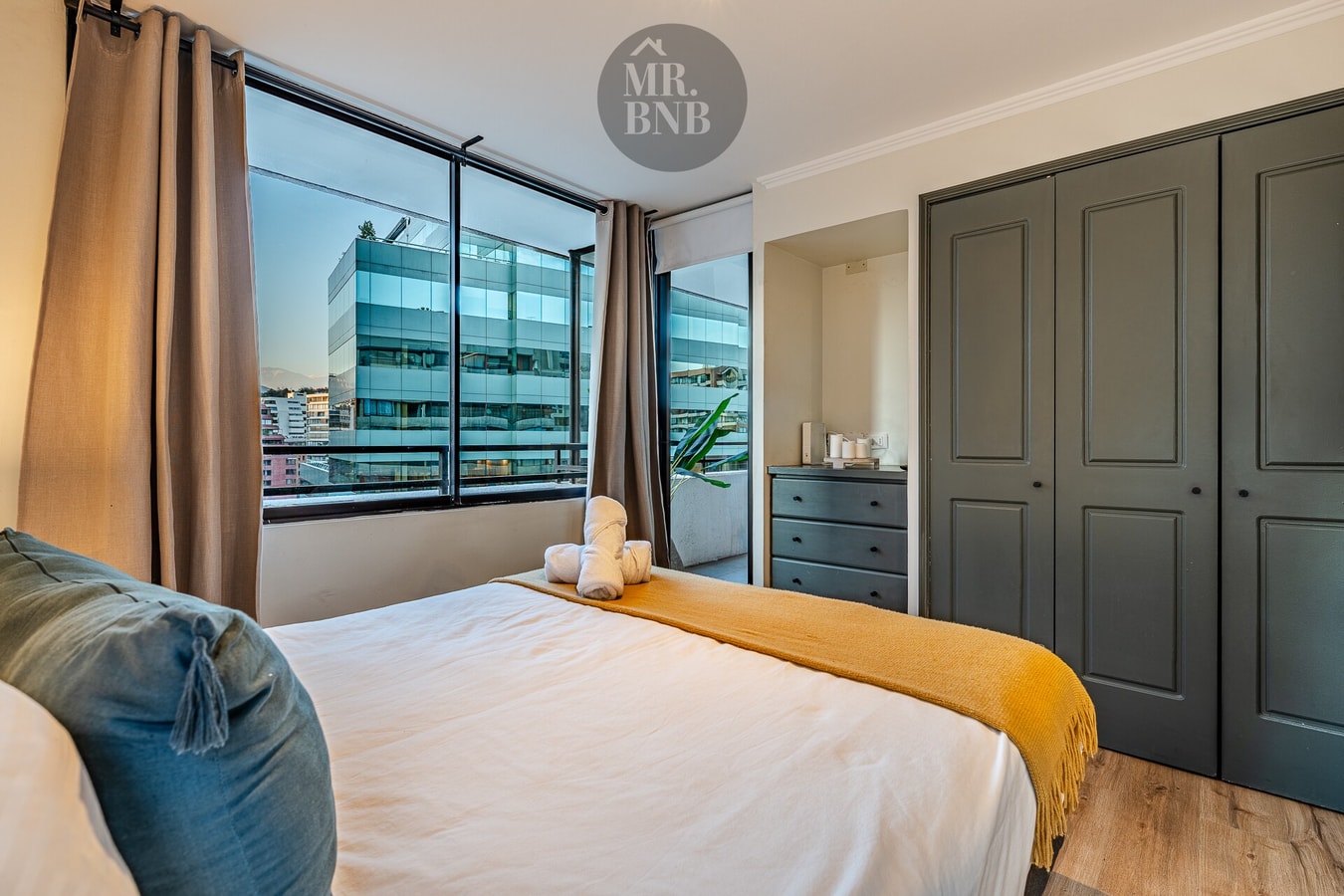Dormitorio con cama de dos plazas, clóset de puertas oscuras y ventana con vista urbana