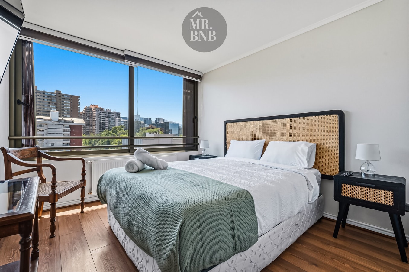 Dormitorio con cama, escritorio y silla, ventanal con vista a la ciudad.