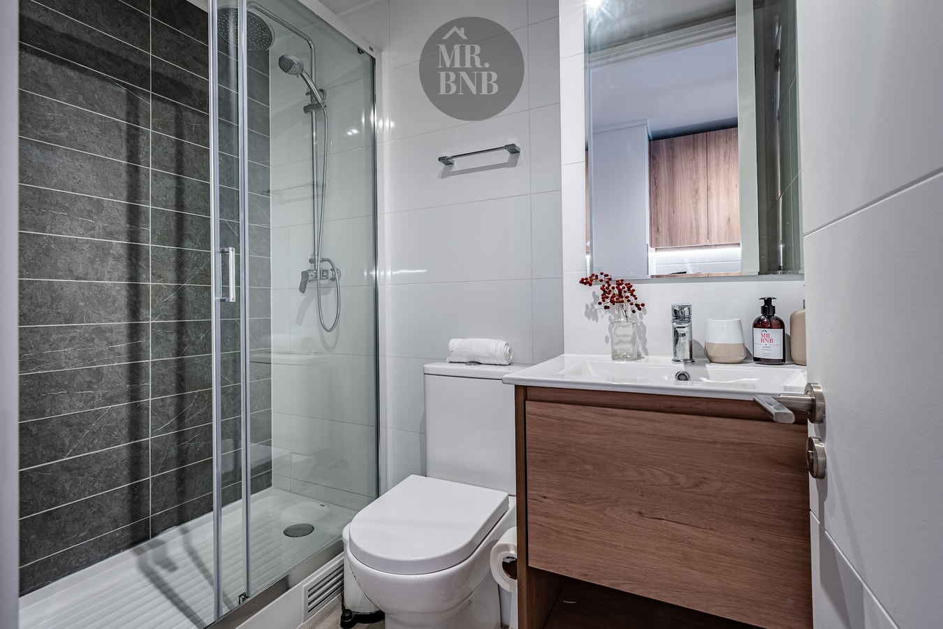 Baño con ducha de vidrio, mueble de madera con lavamanos e inodoro