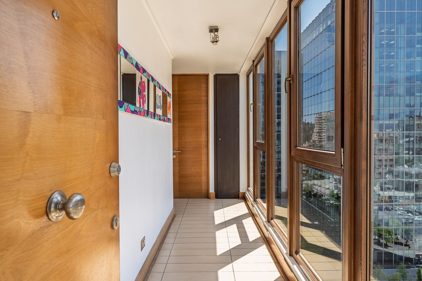 Pasillo interior con ventanales hacia la ciudad y puertas de dormitorios