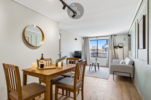 Living comedor con mesa de madera para cuatro personas, espejo redondo y sofá al fondo
