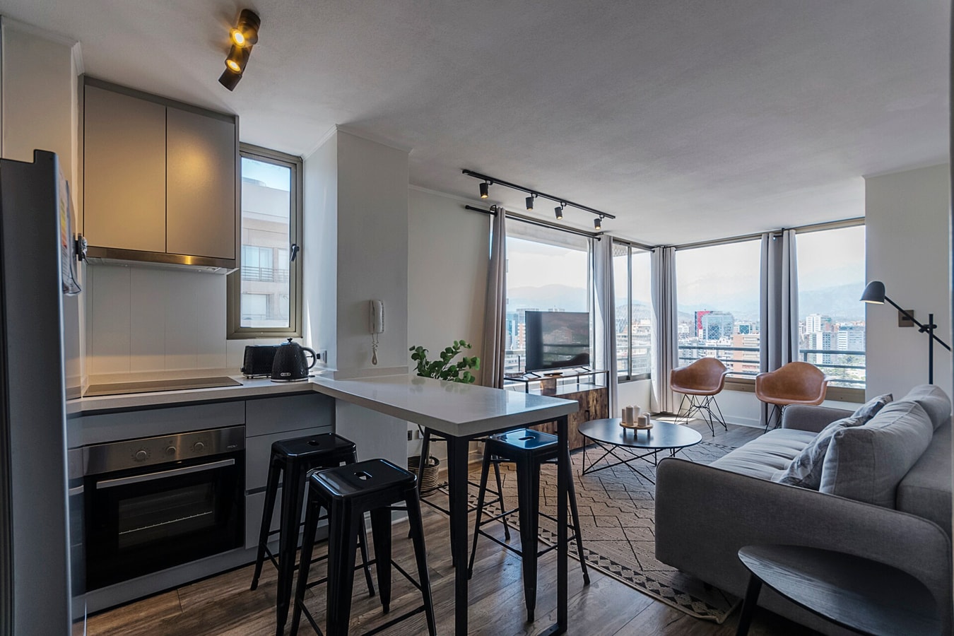 Living con sofá, comedor con mesa alta y sillas, ventanal con vista a la ciudad