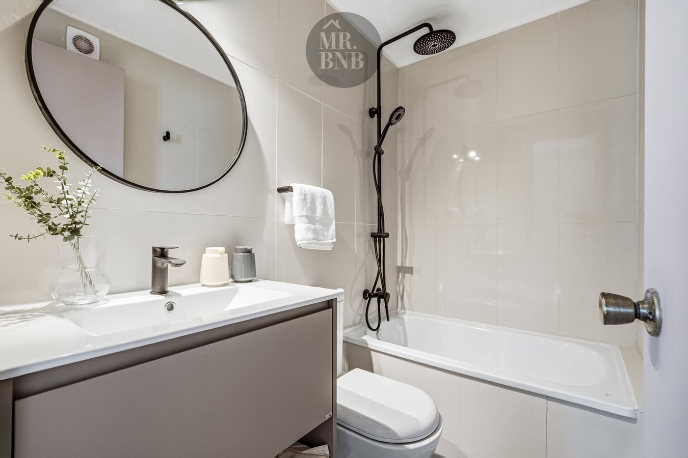 Baño con tina, ducha, espejo redondo y mueble vanitorio