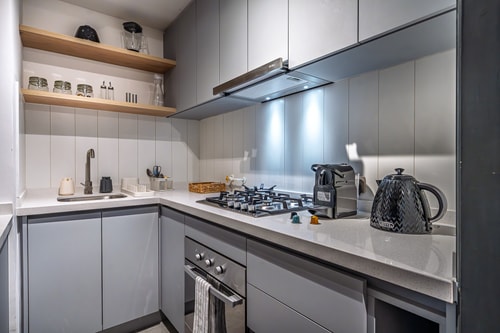 Cocina en L con muebles grises, cocina a gas y repisas abiertas