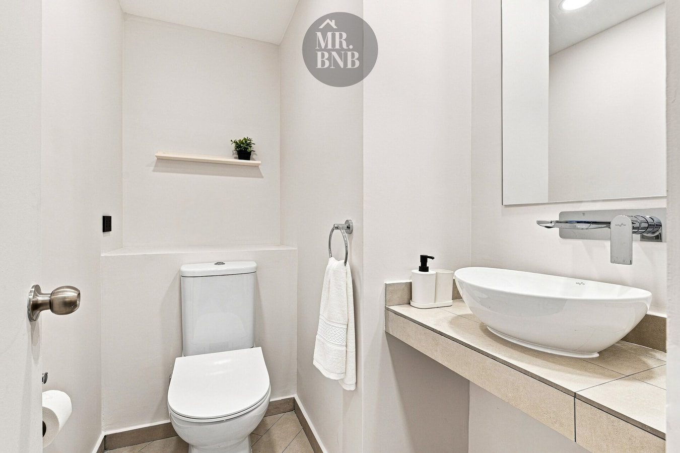 Baño con inodoro, lavamanos ovalado y repisa con amenities.