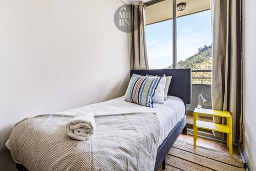 Dormitorio con cama individual, veladores y ventanal con vista al cerro.