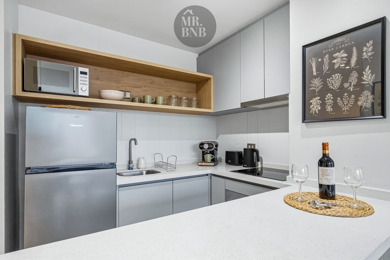 Cocina con refrigerador, microondas, repisa decorativa y botella de vino con copas sobre la encimera