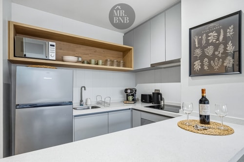 Cocina con refrigerador, microondas, repisa decorativa y botella de vino con copas sobre la encimera