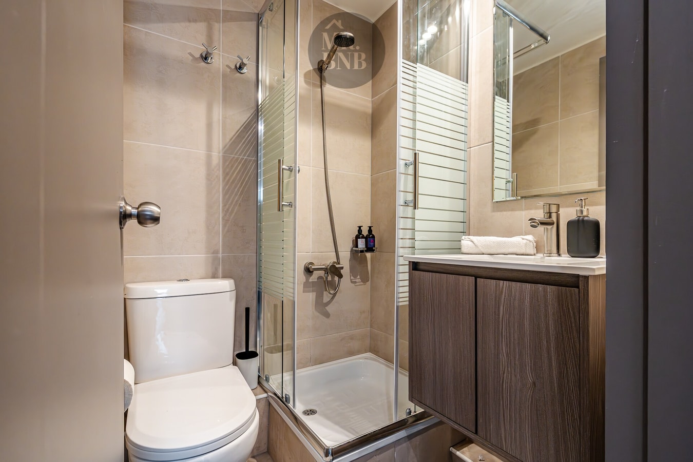Baño con ducha de vidrio, vanitorio de madera e inodoro.